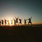 Silhouette of a group of friends jumping on a beach at sunset, expressing joy and freedom.
