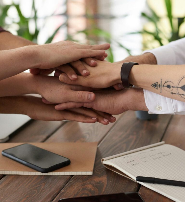 Hands from a diverse team stack on a table symbolizing unity and teamwork in a modern office setting.